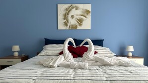Un letto rifatto con biancheria a righe, due asciugamani bianchi disposti a forma di cuore e un cuscino rosso.