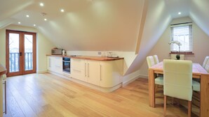 A spacious kitchen with wooden flooring, a dining area with a table and chairs, and a large window with blinds. - Comfortable Cosy Private Barn conversion, Own courtyard, parking, nr to station (Hertford)