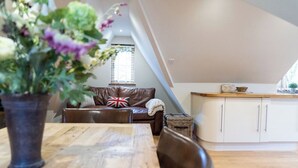 A cozy loft apartment with a dining area, a sofa with a Union Jack pillow, and a kitchen with white cabinets. - Comfortable Cosy Private Barn conversion, Own courtyard, parking, nr to station (Hertford)