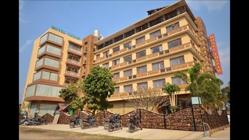 A multi-story hotel with balconies, a parking area with motorcycles, and a stone wall.
