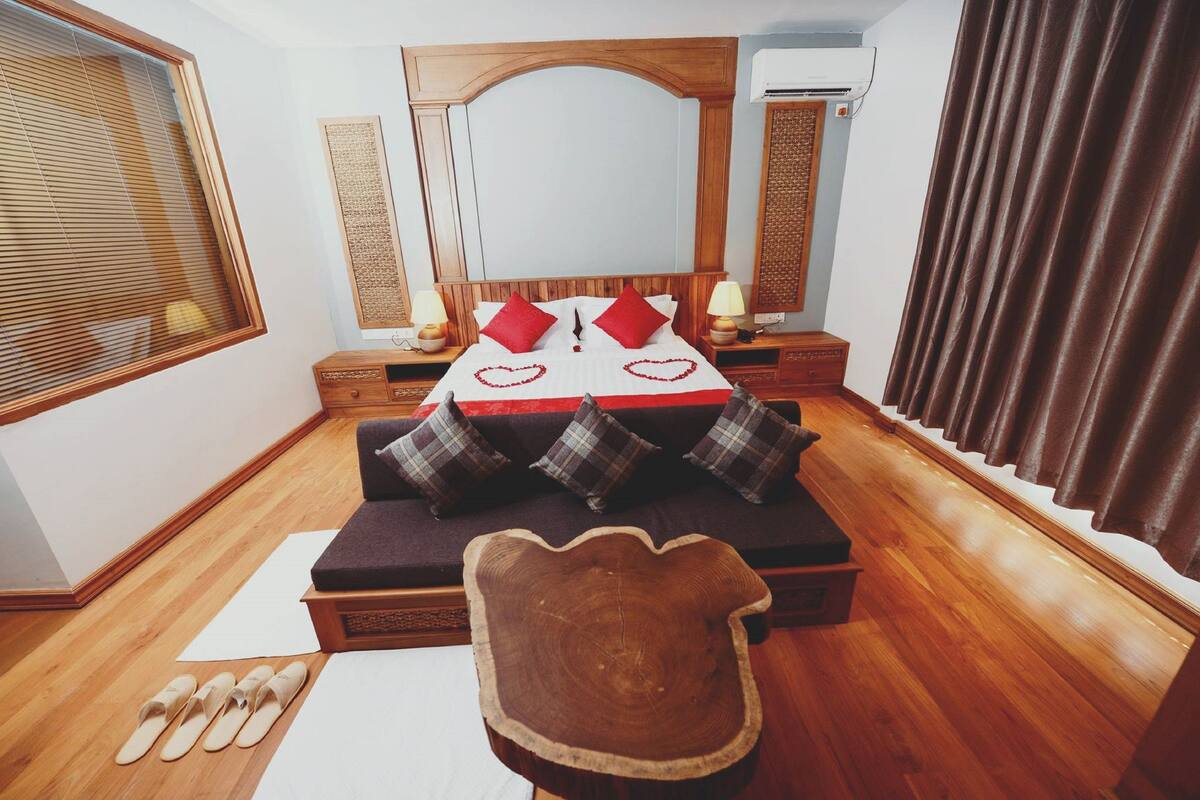 A bedroom with a wooden bed, a nightstand, a dresser, a wooden chair, and a window with blinds.