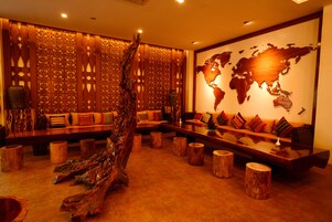 A modern lounge area with a large wooden sculpture, a world map on the wall, and a long wooden bench with colorful cushions.