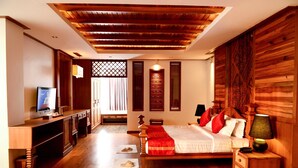Una habitación de hotel con techo de madera, una cama con ropa de cama roja y blanca, una mesita de noche con una lámpara y un televisor sobre un mueble de madera.