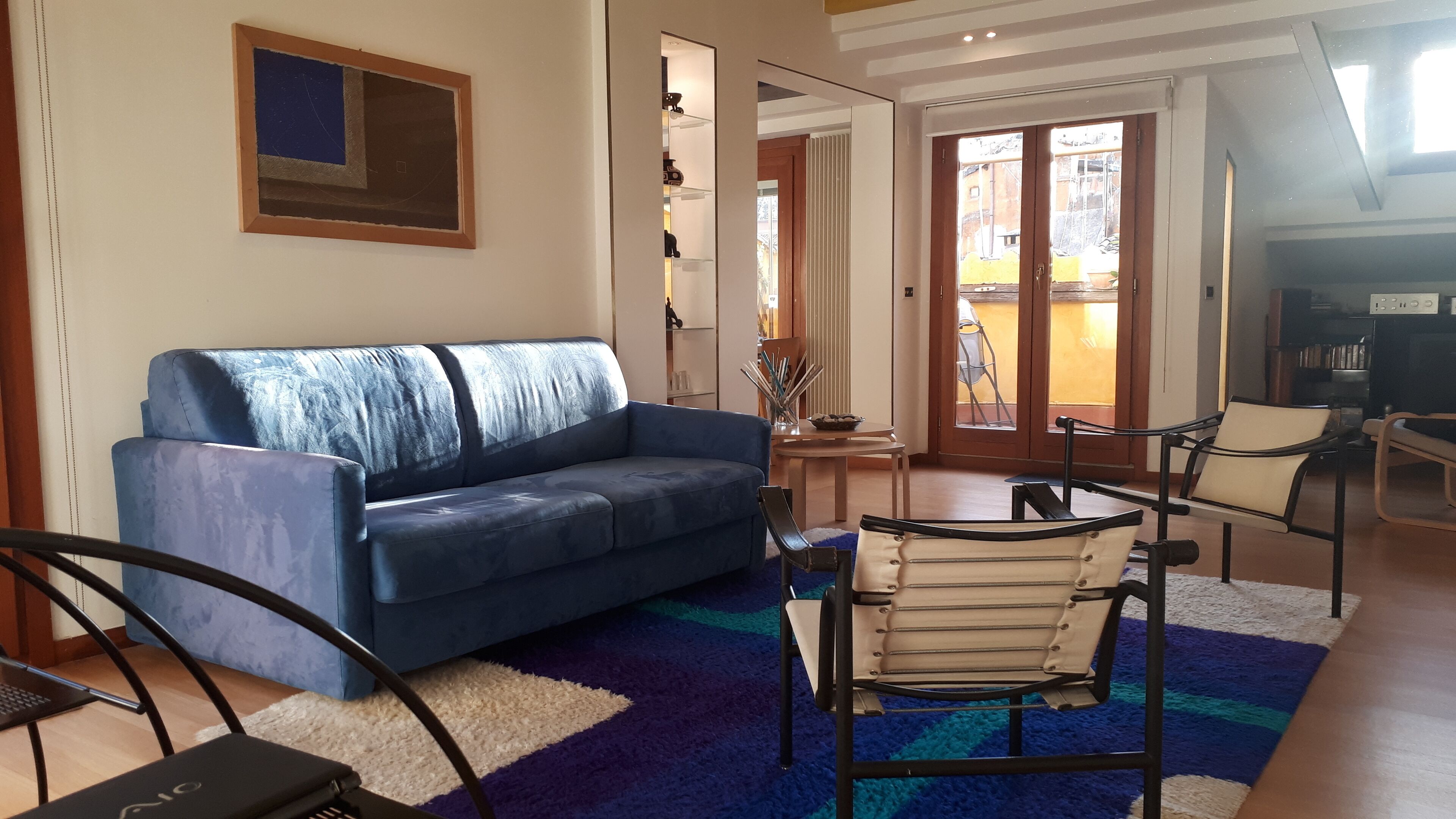 A living room with a blue sofa, a small table with a vase, and a chair.
