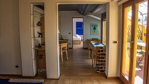 A hallway with a wooden floor leading to a dining area with a table and chairs. There is a bookshelf with various items on it, and a door leading to another room. - Attic of great charm with terraces and panoramic views (Roma)