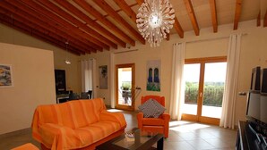 Ein geräumiges Wohnzimmer mit Holzbalkendecke, einem großen Fenster mit Blick und einem modernen, orangefarbenen Sofa.