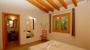 Ein Schlafzimmer mit Bett, einem Fenster mit Blick auf Bäume, einem Spiegel und einem durch eine offene Tür sichtbaren Badezimmer.