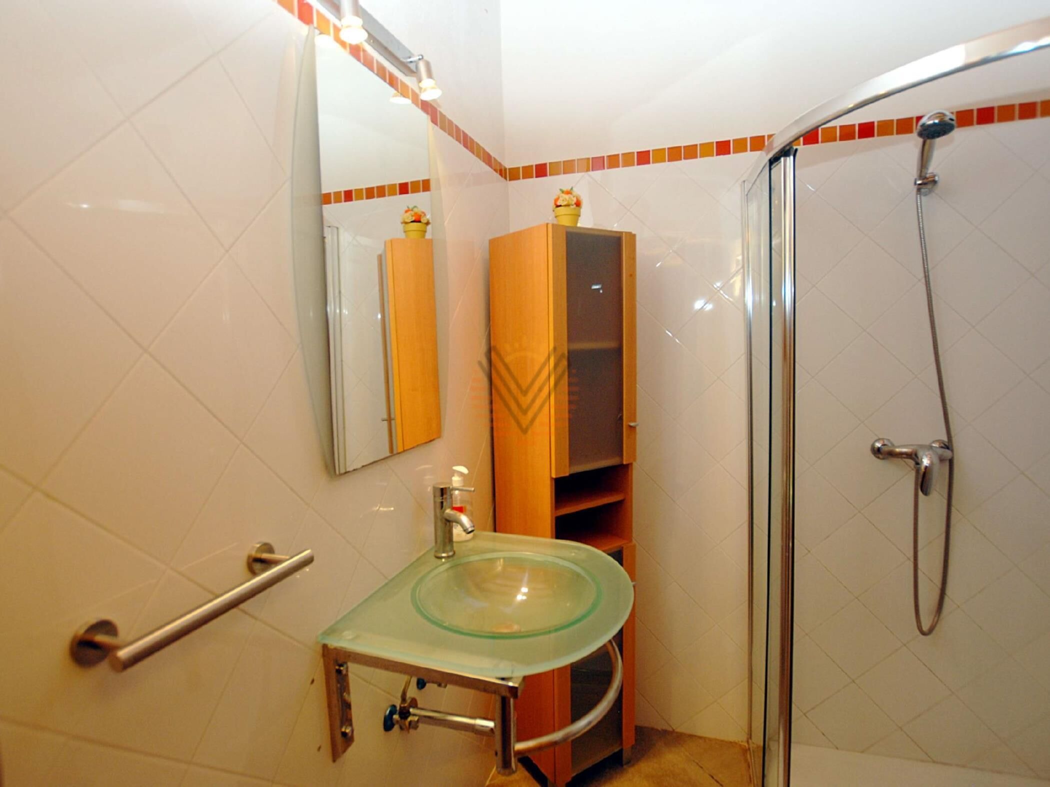 Un baño con lavamanos de vidrio, un espejo, ducha y perchero para toallas.