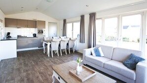 A modern kitchen with grey cabinets and a dining area with a white table and chairs. - EuroParcs Spaarnwoude (Halfweg)
