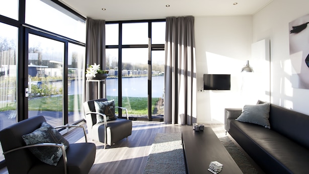A modern living room with a large window, a sofa, a chair, and a flat-screen TV. - EuroParcs Spaarnwoude (Halfweg)