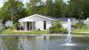 A white mobile home with a patio, a small garden, and a pond with a fountain. - EuroParcs Spaarnwoude (Halfweg)