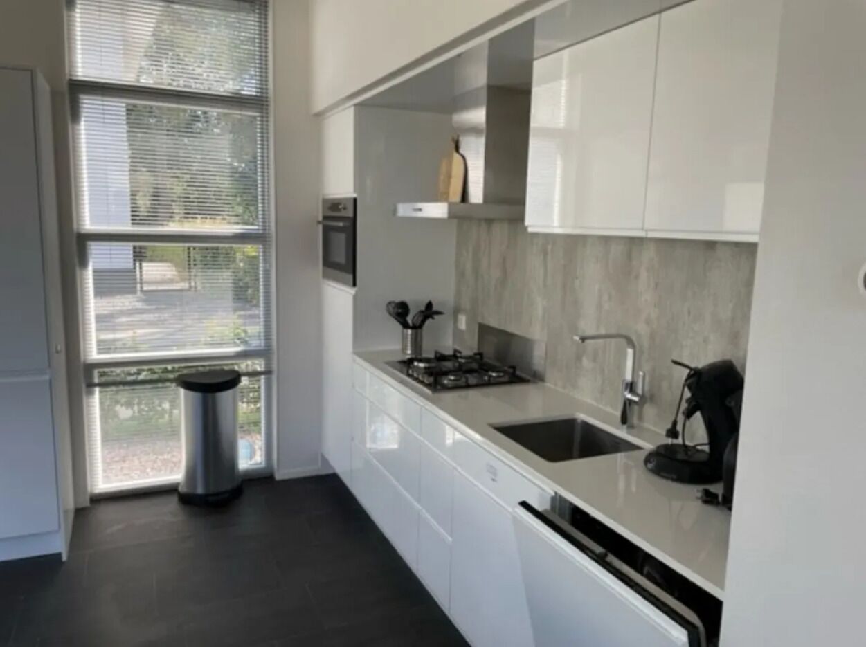A modern kitchen with white cabinets, a stainless steel sink, and a window with blinds.