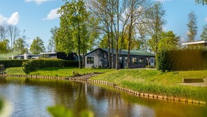 A modern house with a pond in front, surrounded by trees and a grassy area. - EuroParcs Spaarnwoude (Halfweg)