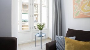 A modern living room with a sofa, a small round table with a vase of flowers, a balcony door, and a painting on the wall. - Singular Stays Mar44 III (Valencia ciudad)
