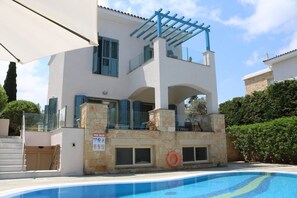 A two-story building with a pool, stone pillars, and a pergola.