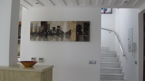 Un intérieur moderne avec un escalier blanc, un tableau accroché au mur et un bol posé sur un comptoir.
