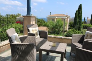 Une terrasse dotée de meubles en osier, une table avec une bougie et une vue sur la mer et les bâtiments.