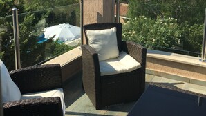 Un balcon agrémenté de meubles en osier, d’un parasol blanc et offrant une vue sur l’océan et les bâtiments.