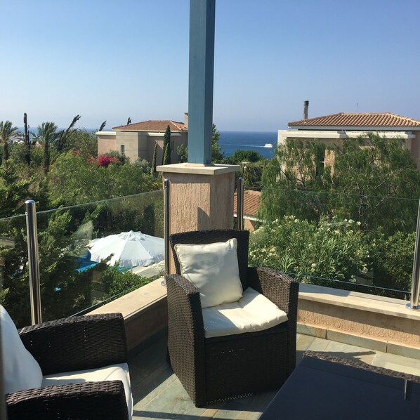 A balcony with wicker furniture, a white umbrella, and a view of the ocean and buildings.