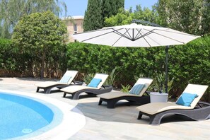 Un espace aménagé au bord de la piscine, avec des chaises longues et un grand parasol.