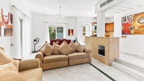 A modern living room with a beige sofa, a dining area, and a kitchen with a wooden cabinet.