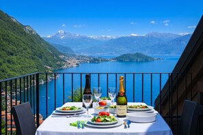 A table set with plates, glasses, and a bottle of champagne, overlooking a lake with mountains in the background. - Residence Eden Magnolia 19, Argegno, Italy (Argegno)