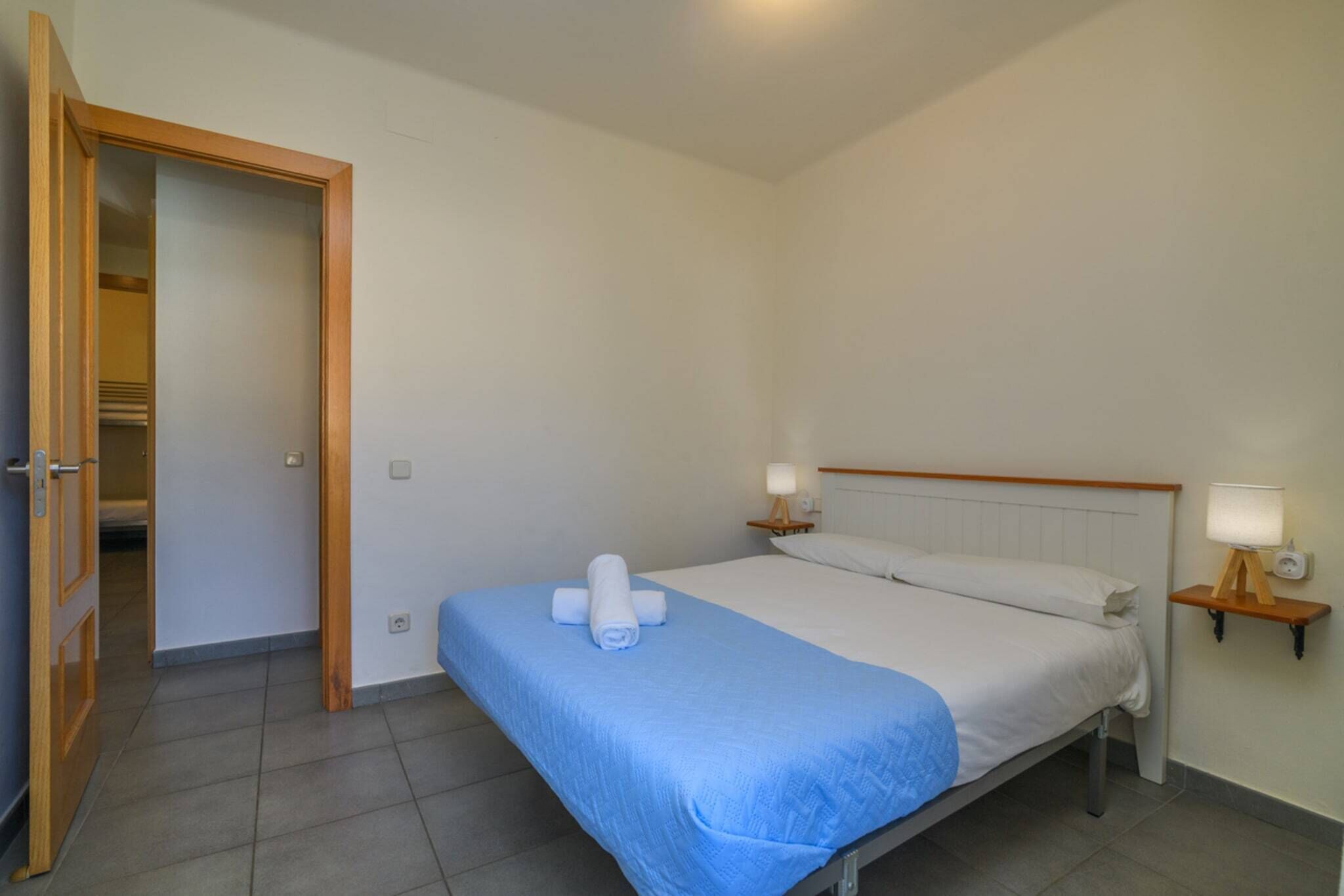 Una habitación de hotel con una cama, dos lámparas de noche, una puerta de madera y una mesita auxiliar.