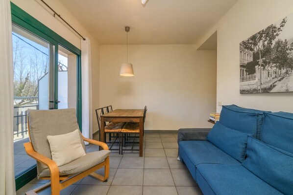 Une pièce comprenant une table à manger en bois, un canapé bleu, une chaise, un luminaire suspendu et un tableau encadré accroché au mur.