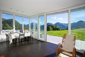 A dining area with a table set for two, large windows offering a mountain view, and a wicker chair.