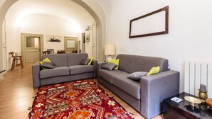 Ein Wohnzimmer mit zwei grauen Sofas, einem gemusterten Teppich, einem Tisch mit einer Lampe und einem gerahmten Bild an der Wand.