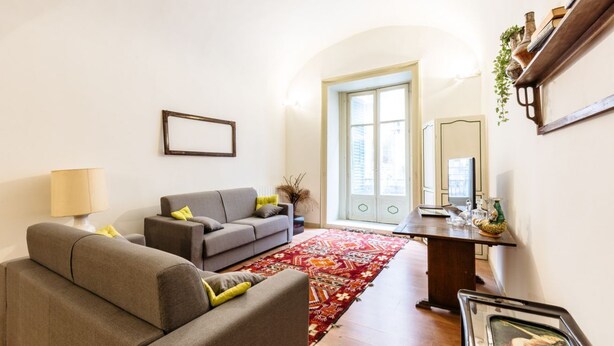 Ein Wohnzimmer mit einer Couch, einem Couchtisch und einem Teppich. Eine Tür führt in einen anderen Raum.