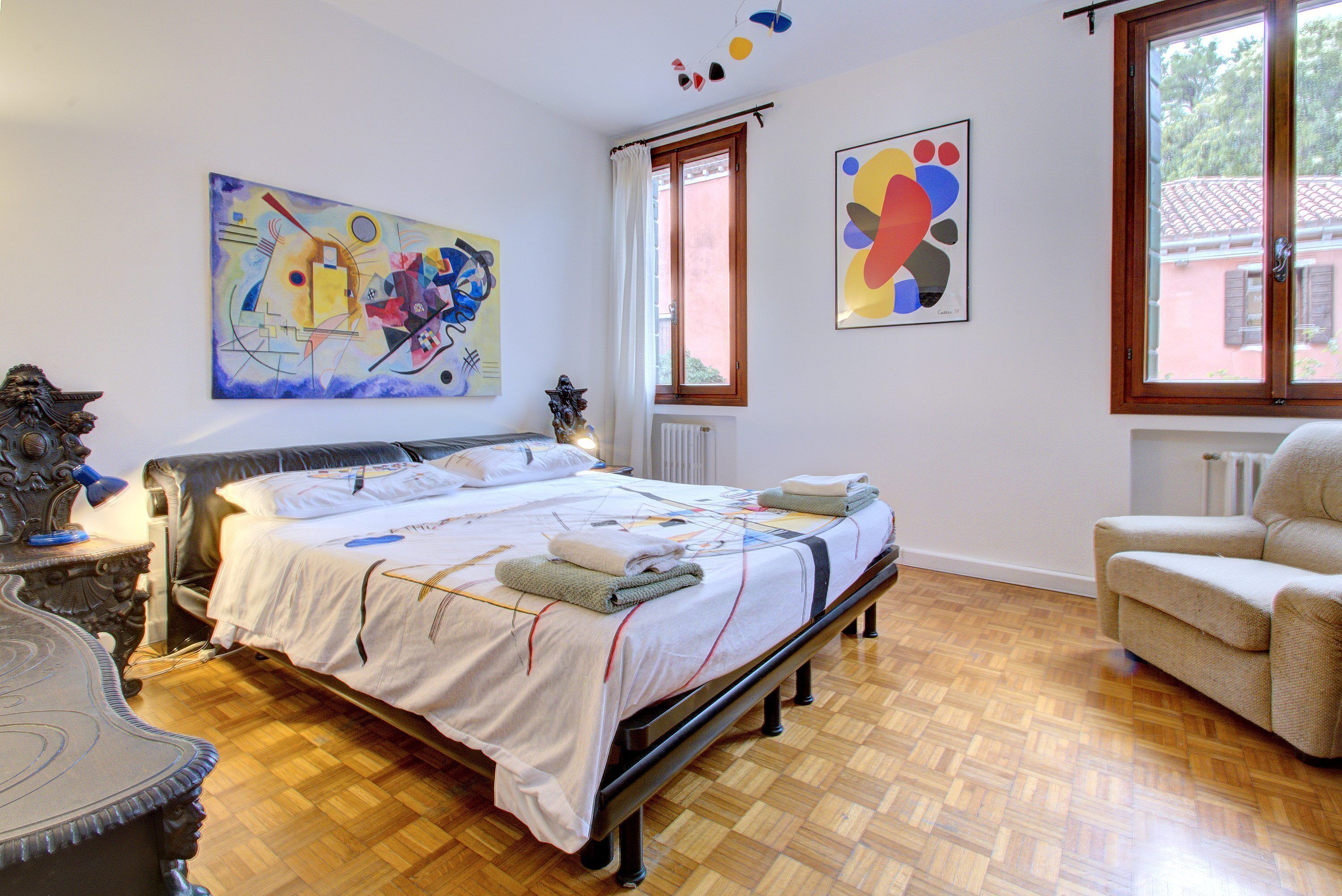 A bedroom with a bed, a chair, and two paintings on the wall.