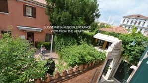 Udsigt fra en lejlighed over mod Guggenheim Museets indgang, med en murstensvæg, grønt og en hvid bygning med et skilt.