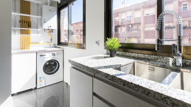 A modern kitchen with a built-in washer, granite countertops, and a large window offering a view of residential buildings. - ApartUP Mestalla Home (Valencia)
