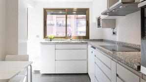 A modern kitchen with a window, granite countertop, and white cabinetry. - ApartUP Mestalla Home (Valencia)
