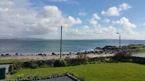 A coastal landscape with a grassy foreground, a stone wall, and a view of the sea and distant hills.