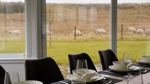 A dining area with a table set for four, overlooking a field with sheep.