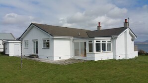 A white two-story house with a grey roof, a covered porch, and a view of the sea.