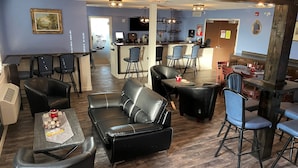 A spacious living area with leather sofas, a dining table, and bar stools. A kitchen area is visible in the background with bar seating. - Travelodge by Wyndham Pincher Creek (Pincher Creek)