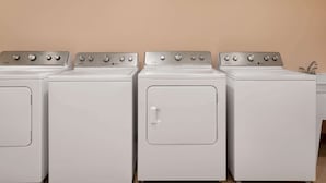 A row of four white front-loading washers with control panels, set against a plain wall. - Travelodge by Wyndham Pincher Creek (Pincher Creek)
