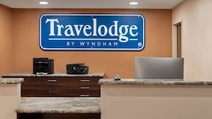 A reception area with a blue sign reading "Travelodge by Wyndham" above a counter with a coffee machine and a TV. - Travelodge by Wyndham Pincher Creek (Pincher Creek)