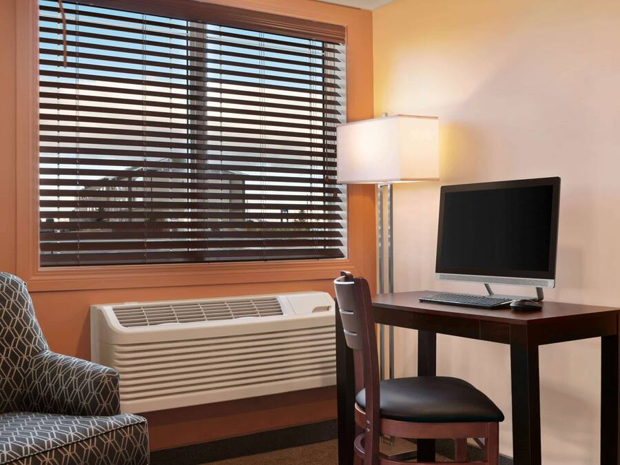 Ein Hotelzimmer mit Schreibtisch, Computer, Stuhl und Klimaanlage.