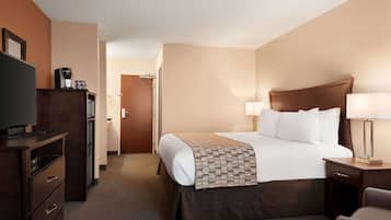 Habitación de hotel con cama, mesita de noche, lámpara, televisor y escritorio con cajones.