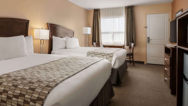 A hotel room with two beds, a desk, a chair, a TV, and a wardrobe. - Travelodge by Wyndham Pincher Creek (Pincher Creek)