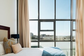 Een hotelkamer met een groot raam, een bed met kussens en een nachtkastje met een lamp.
