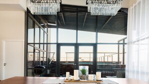 A dining area with a wooden table, black chairs, and a view through large windows to an outdoor patio. - Hillhouse Penthouse 7th Floor (Cape Town)