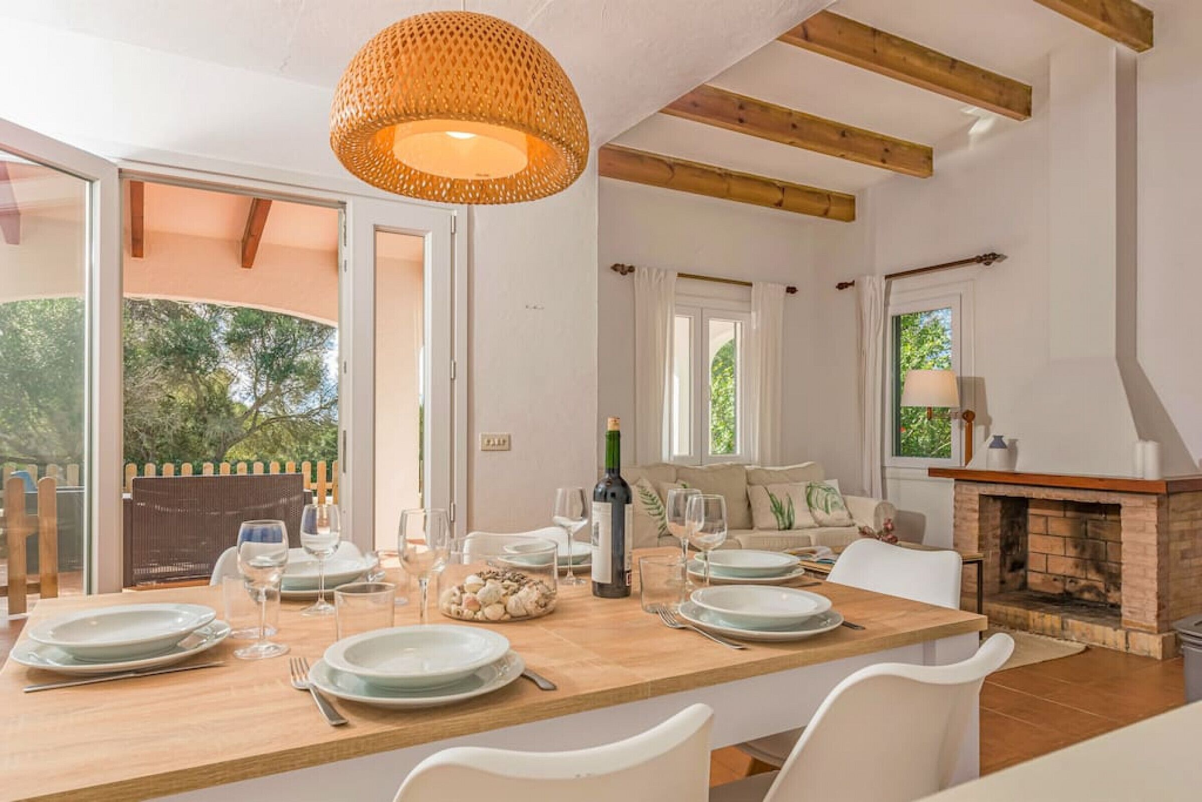 Uma sala de jantar com uma mesa de madeira posta para quatro pessoas, uma garrafa de vinho e uma lareira.
