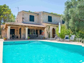 Une villa en pierre dotée d’une piscine, d’un espace salon extérieur et d’une pergola.