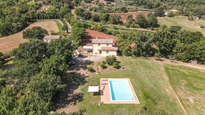 Una proprietà su una collina con piscina, una casa grande e vegetazione circostante.