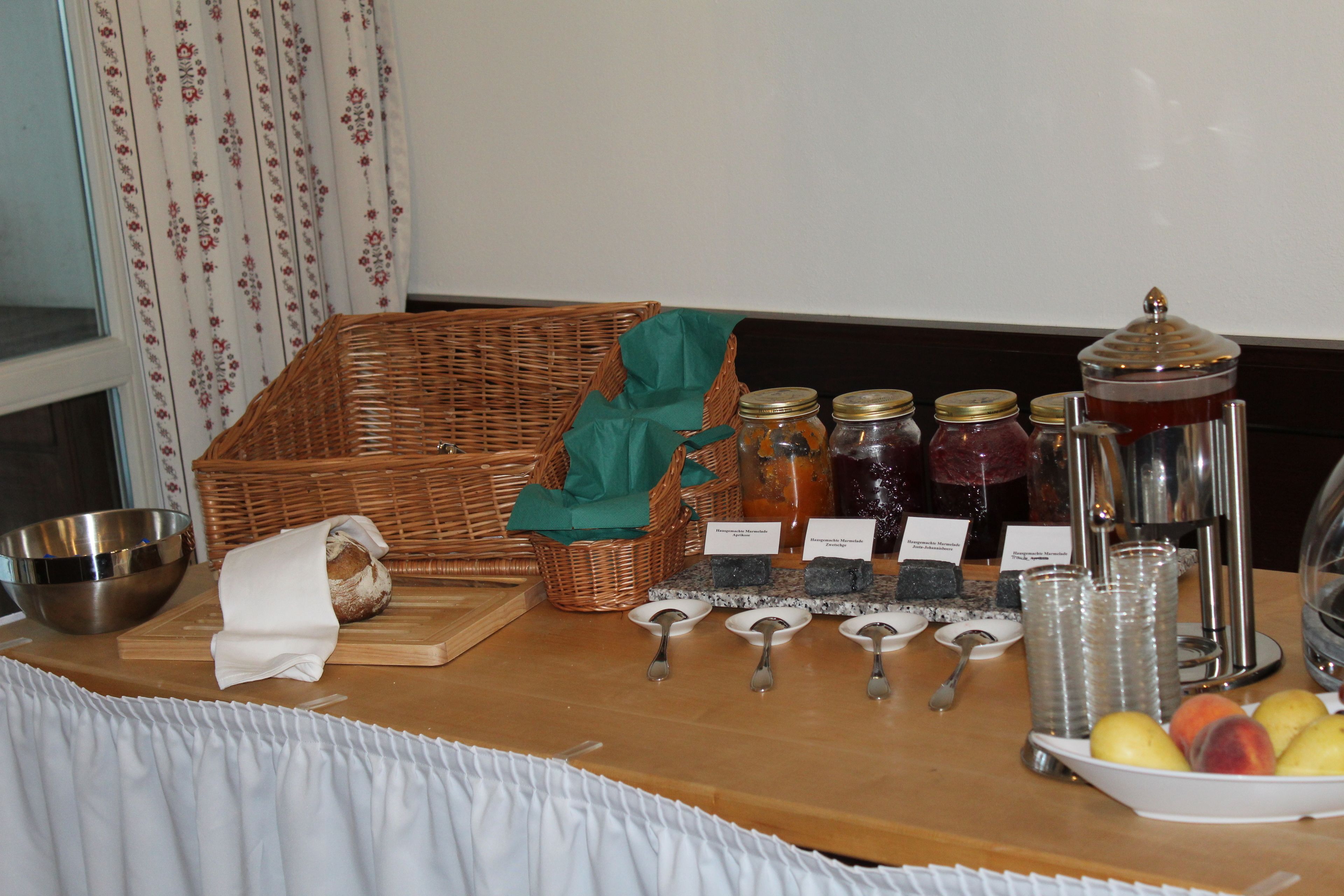 A buffet setup with a wicker basket, jars of condiments, a bowl of fruits, and serving utensils.